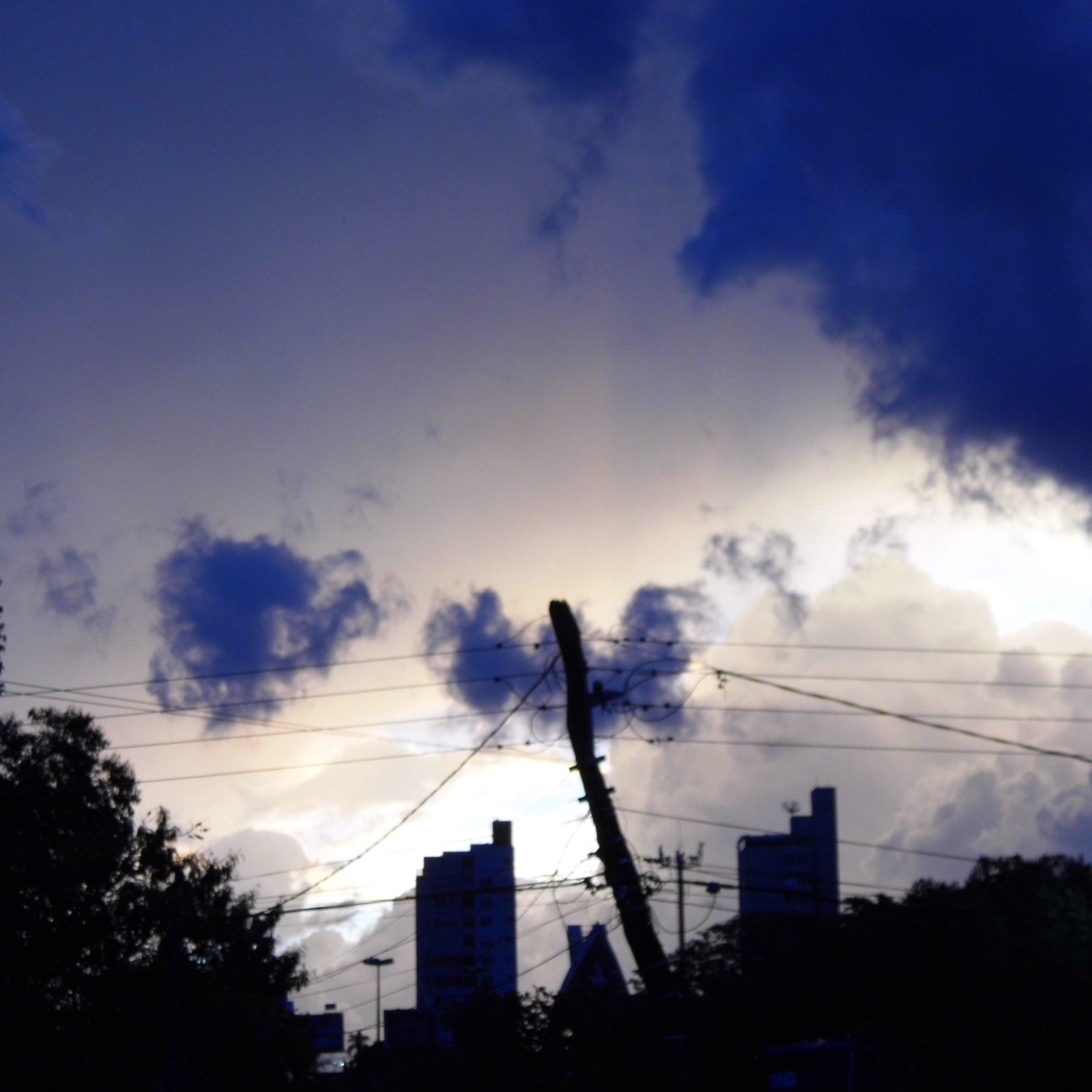 Céu dramático de tempestade em contraluz sobre silhuetas de prédios e um poste torto